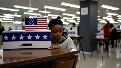 people interacting with a ballot box adorned with an american flag at a polling place