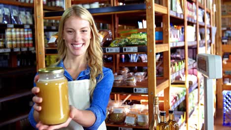 smiling female staff holding jar of honey in supermarket