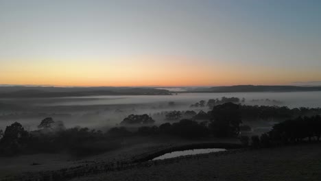 aerial moving forward low over farm land in australia with mist and fog over the land in winter