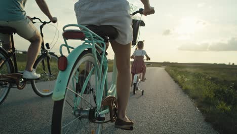 Rear-view-of-family-of-four-caucasian-people-riding-bikes-on-village-road.