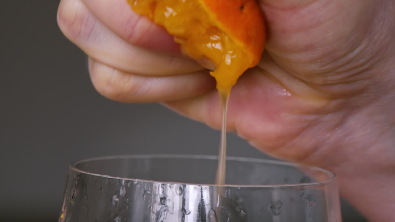 A woman squeezes juice from an orange into a glass. Slow motion