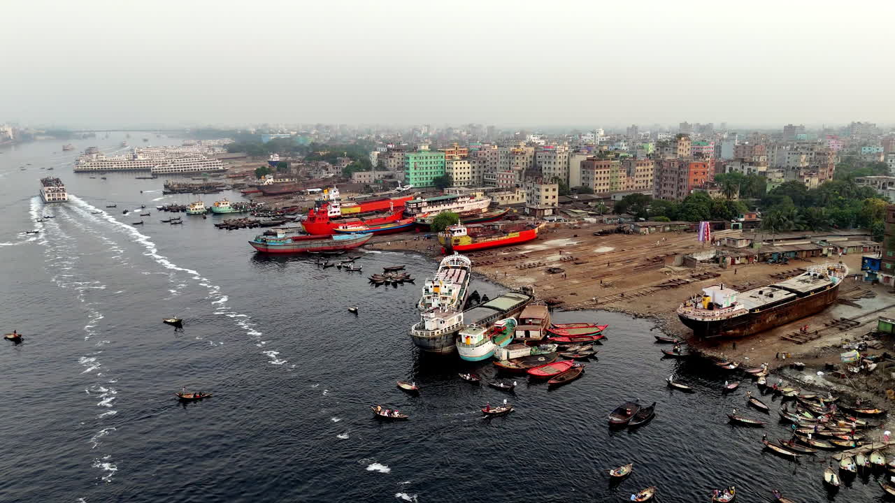 Cinematic aerial drone shot approaching the large cargo ships docked on the shore of the Buriganga river in Dhaka, Bangladesh