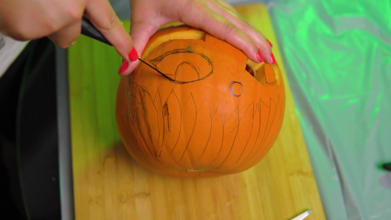 el ojo de calabaza está siendo tallado en una tabla de cortar dentro de la casa con luz verde