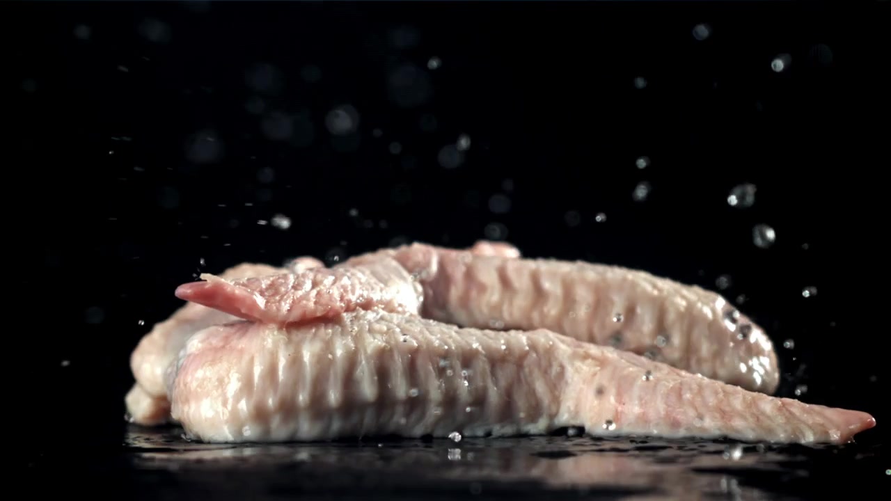 Rohe Hähnchenflügel fallen in Zeitlupe und spritzen Wasser