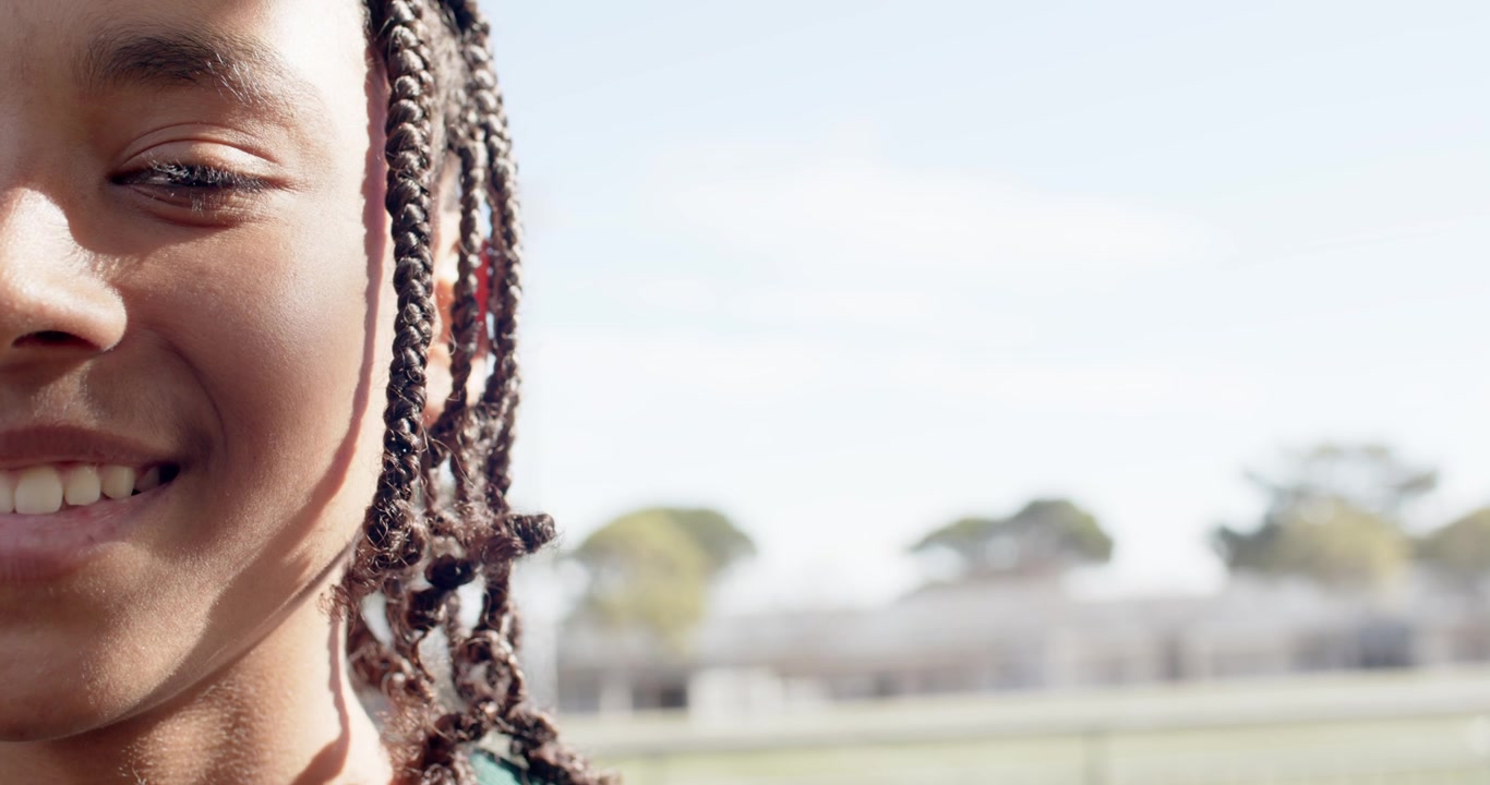 Adolescente afroamericano sorridente, che allarga la bocca dopo aver girato la testa, su un campo, con le treccine, spazio per il testo.