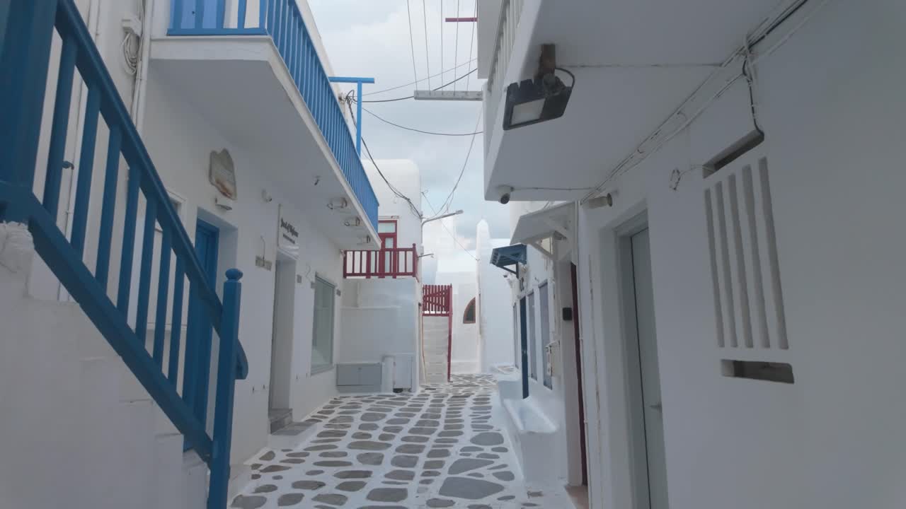 A cinematic walking pullback moves through the whitewashed alleys of Mykonos in winter, capturing the serene architecture, narrow streets, and charming island atmosphere