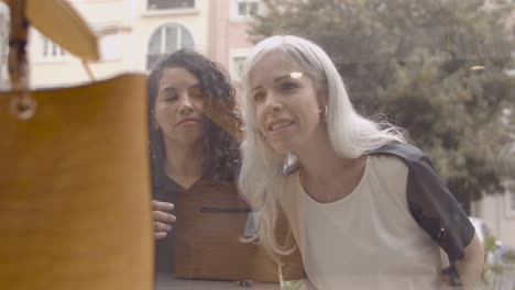 cheerful female shoppers staring at accessories in shop window