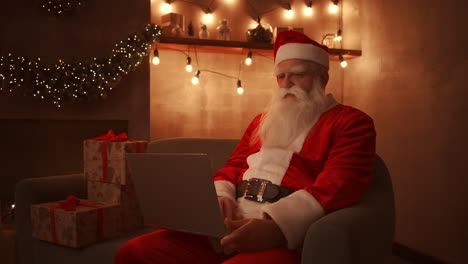 Santa-Claus-is-working-on-a-laptop-sitting-at-home-on-the-sofa-in-the-background-of-Christmas.-Santa-responds-to-children-emails.-High-quality-4k-footage