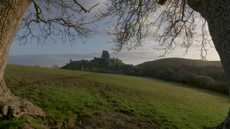 slow zoom in shot of corfe castle framed by trees in the early morning light