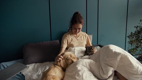 a brunette girl lies on a bed near her dog and cat. the cat does not like the presence of the dog, but the girl reconciles them. interact pets at home