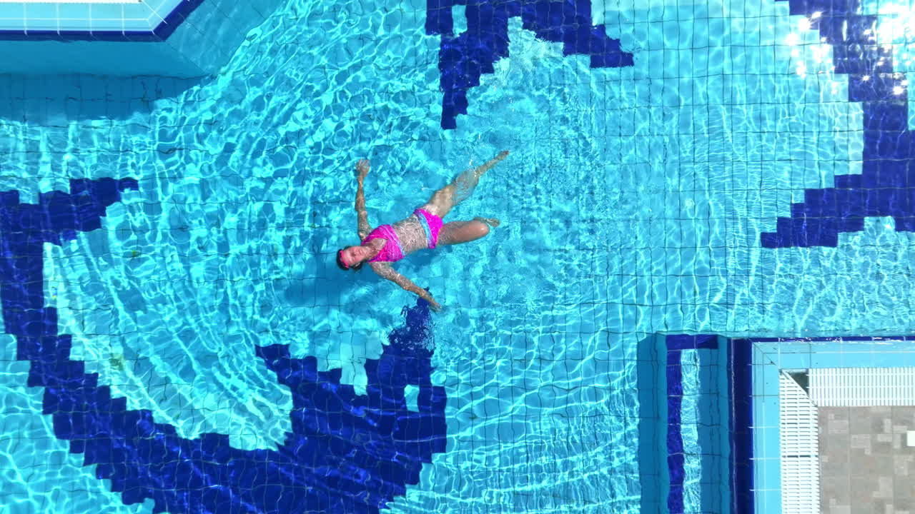 Cenital drone shot above a woman floating on her back in a pool at a villa