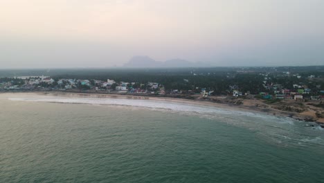 un dron aéreo filmado sobre kanyakumari capturando la fascinante mezcla de luces de la ciudad y olas del océano al anochecer.