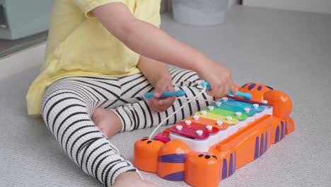 one 3-year-old korean-ukrainian little girl plays on toy tikes jungle jamboree tiger piano xylophone at home sitting on floor