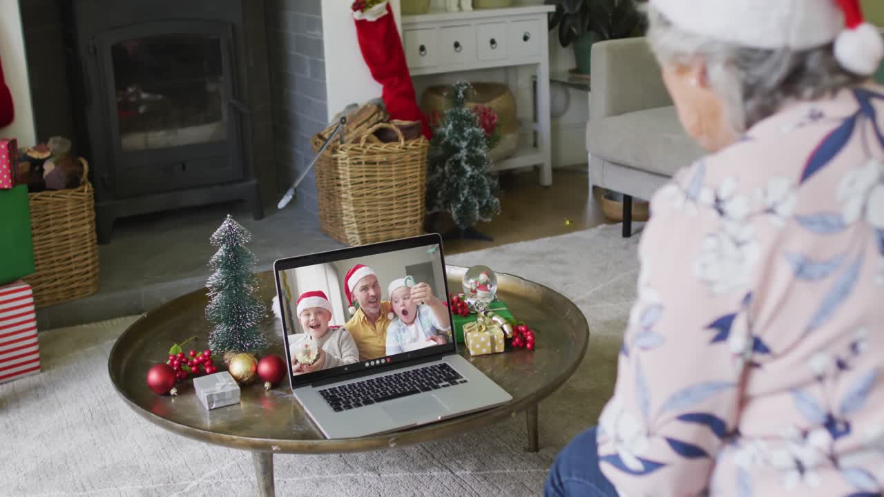 mujer mayor caucásica con sombrero de santa usando una computadora portátil para una videollamada de navidad con la familia en la pantalla