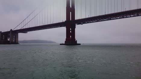 gimbal close-up and tilting up shot from a moving boat as it approaches the underside of the golden gate bridge on a foggy day
