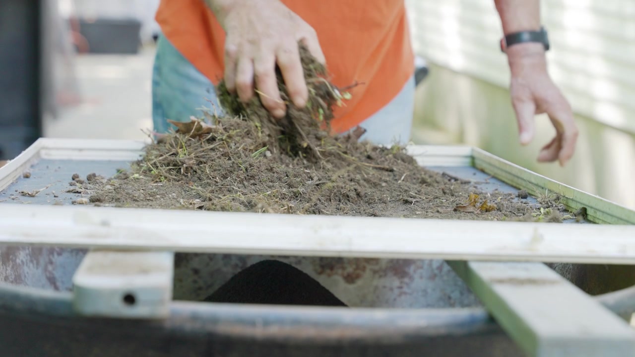 Gardener's hands shaking and sifting soil with a screen sieve to remove roots, rocks and debris
