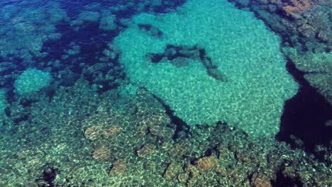 Luftaufnahme-Von-Felsen-Und-Einem-Klaren-Blauen-Meer,-Das-Unterwasserriffe-Enthüllt