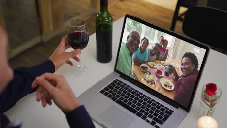 sección media de una mujer afroamericana bebiendo vino mientras hace una videollamada en una computadora portátil en casa