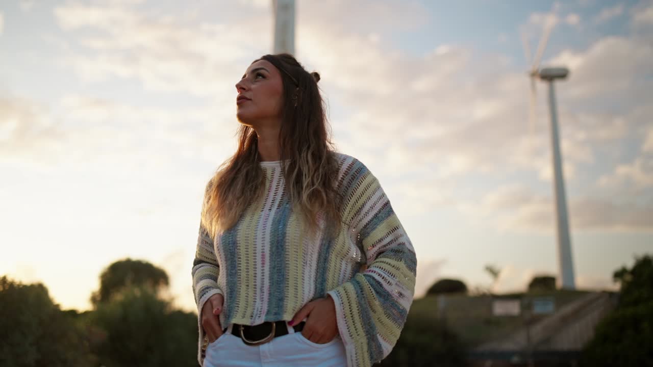 Woman standing in front of wind turbines at sunset