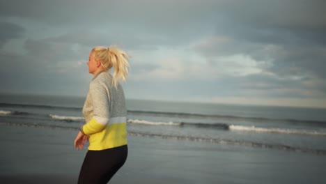 Junge-Blonde-Frau-Läuft-Sportlich-Am-Ufer-Entlang-Und-Blickt-Lachend-Zurück