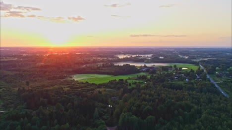 Aerial-view-over-a-mixed-landscape-of-forests-and-fields-under-an-orange-sunrise