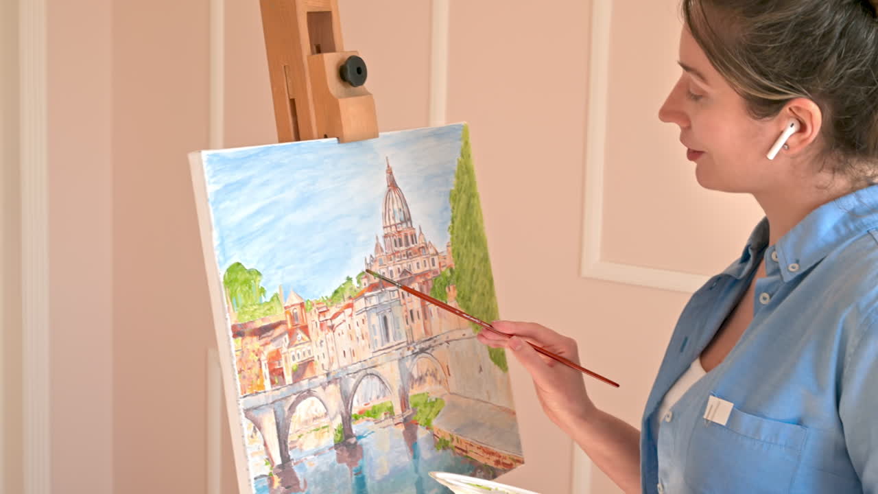 Caucasian woman painting a picture with a palette in her hands and listening music with earphones indoors