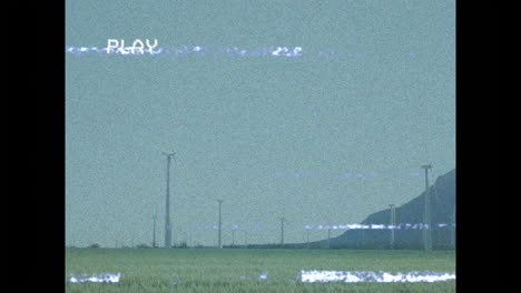animation of vhs-style static with play text over landscape with distant hills