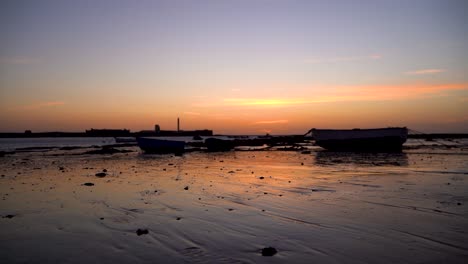 Stunning-sunset-low-angle-view-of-small-silhouetted-fishing-boats-and-reflections