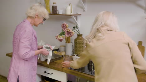 vista trasera de dos mujeres maduras secando platos y cubiertos para una cena familiar en la cocina mientras hablan y ríen