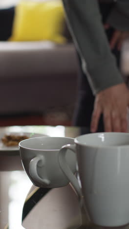 video vertical de primer plano de bebidas calientes en tazas en la mesa en casa con bocadillo con persona en el fondo 1