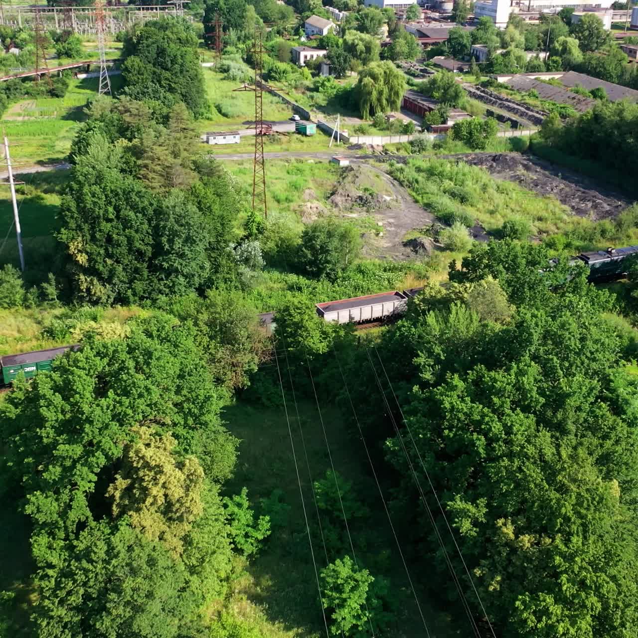 Freight train passing on railway. Cargo train with freight wagons moving among green nature in summer. Aerial view.