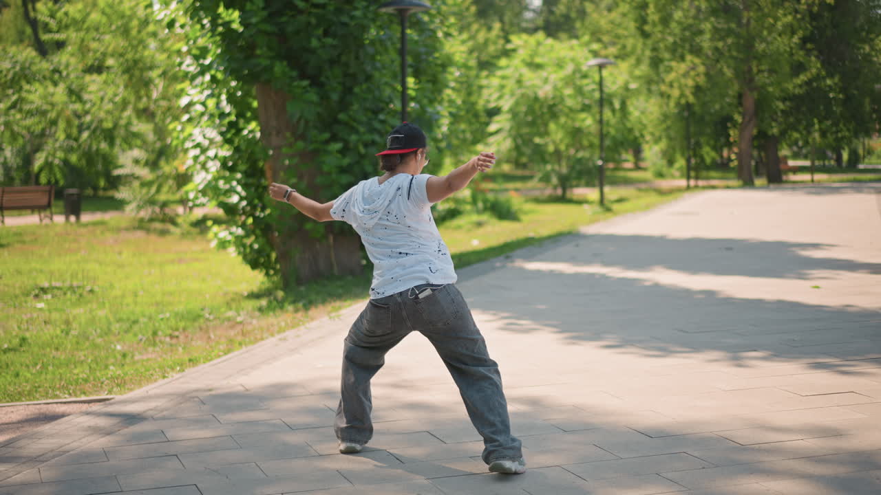 강 다리 근처의 길에서 활기차게 점프하는 남성, 공중에서 비틀고 역동적으로 회전하며 운동용 스니커즈와 모자를 착용, 여름의 녹음이 우거진 곳에서 표현력이 풍부한 훈련 세션, 고강도 움직임