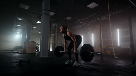 slow motion: a woman lifts a barbell in a dark gym with a lot of weight. a strong young woman lifts weights for a workout