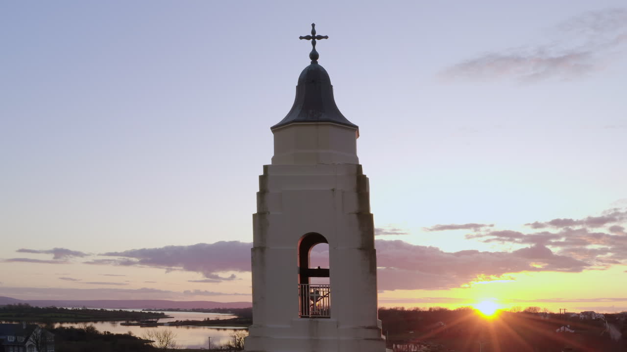 Sunset illuminates church steeple in Clarinbridge with soft gradient sky in warm evening light, backlit flare reveal