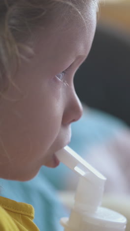 pretty small girl in yellow t-shirt breathes with inhaler lying in bed in light room at home extreme close view