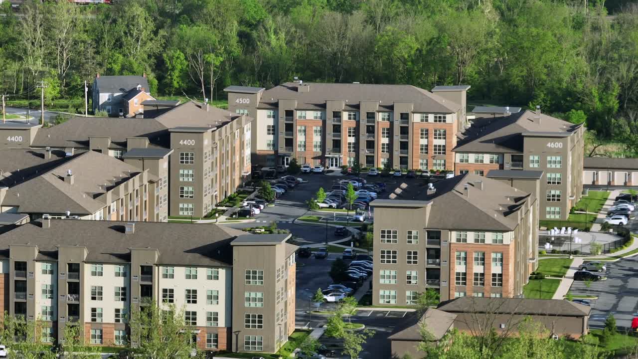 Modern apartment buildings or Multi-family units during sunny day with green trees in spring. Suburb district with parking cars. Aerial approaching shot.