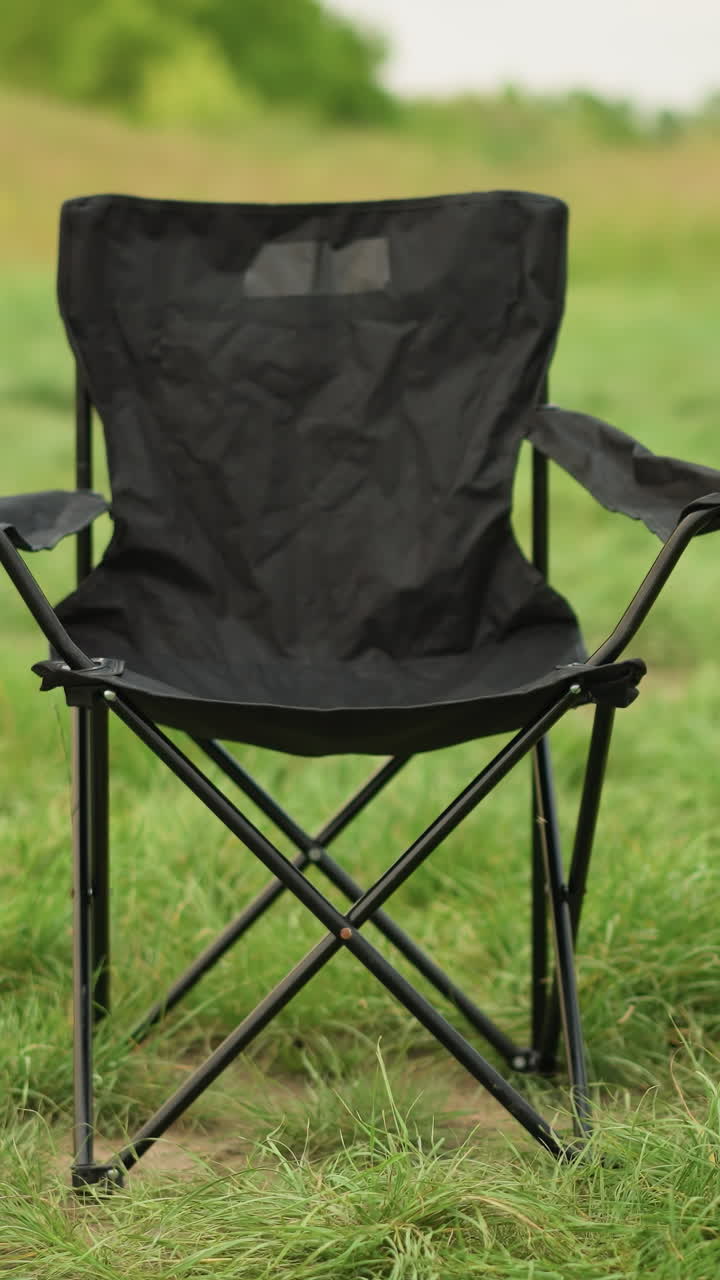 A woman in a white dress reaches out to a black portable chair set on lush green grass, creating a serene outdoor scene