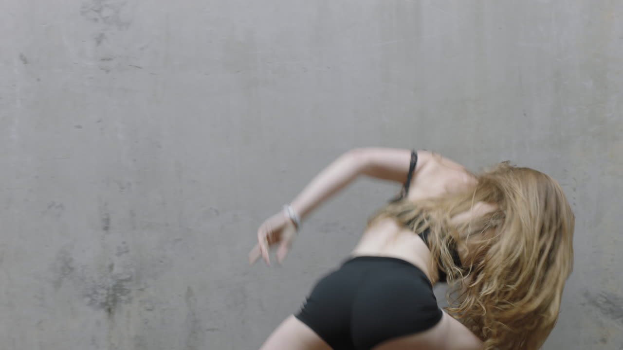 танцующая женщина красивая молодая кавказская уличная танцовщица, исполняющая современные движения, наслаждающаяся современным танцевальным выражением, практикующаяся в грязном складе вблизи