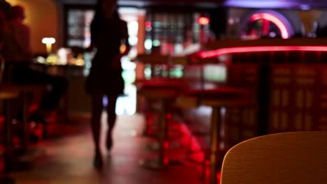 a silhouetted woman enters a contemporary bar with red neon accents, captured in soft focus with moody, low ambient lighting and a stationary camera