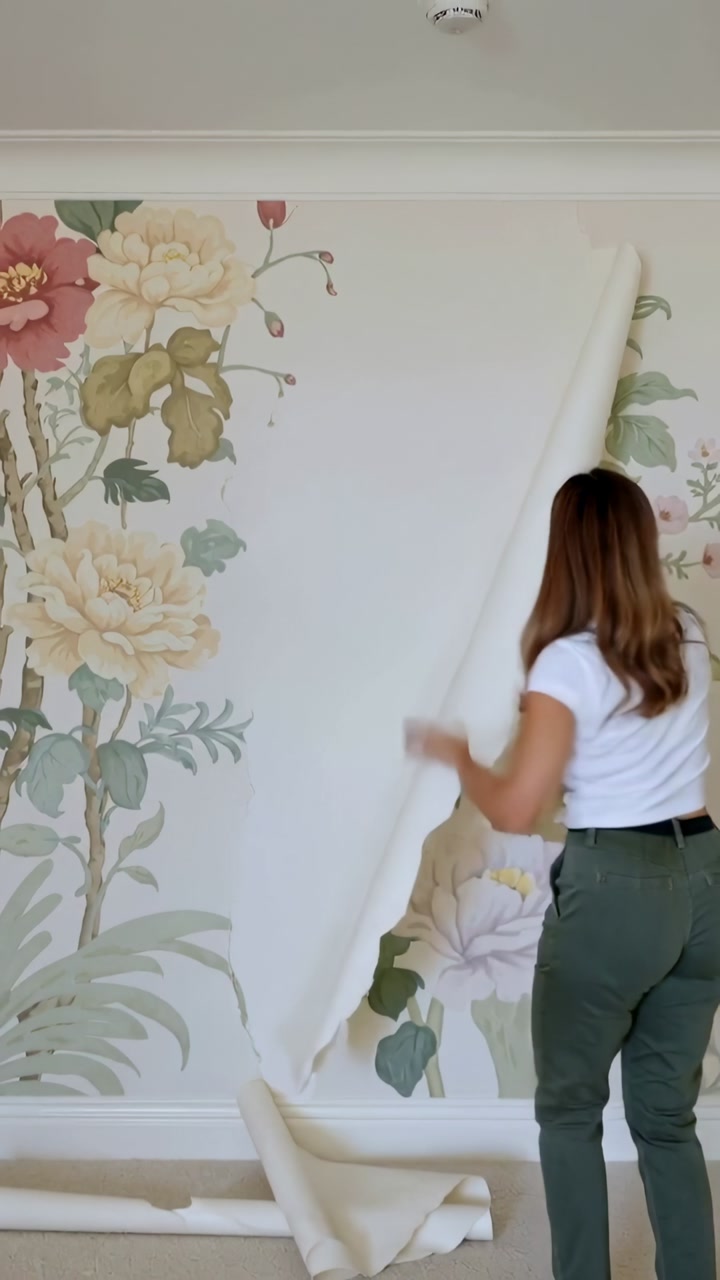 Vertical video: Grabbing top, woman white tee peeling sheet, showing mural at home, copy space