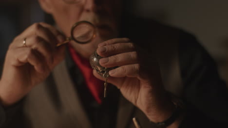 older passionate man evaluates an old silver skull watch in his office at night