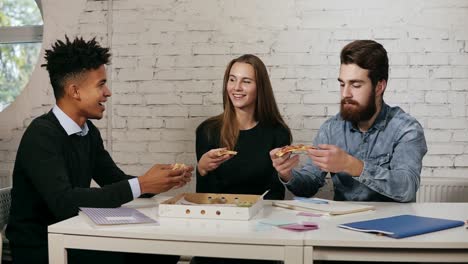 equipo de negocios de jóvenes disfrutando de pizza juntos en la oficina, millennials grupo hablando divirtiéndose compartiendo el almuerzo en acogedor