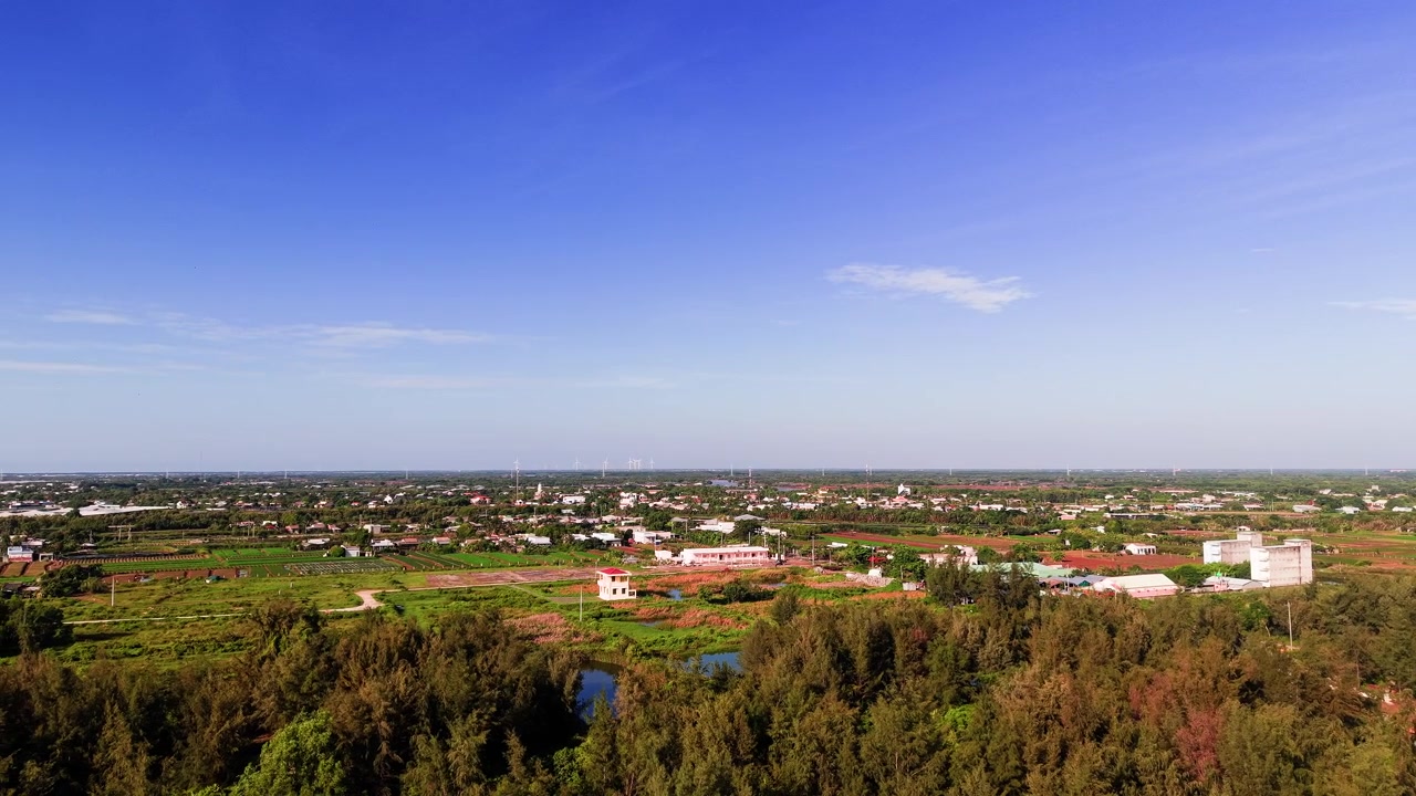 The camera shows a wide view of Thua Duc Beach in Vinh Long, Vietnam. You can see green fields, buildings, and clear skies. It captures the daily life at the beach.
