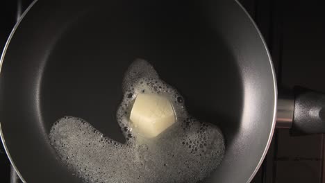 melting butter in a hot black pan - top down tabletop double speed shot