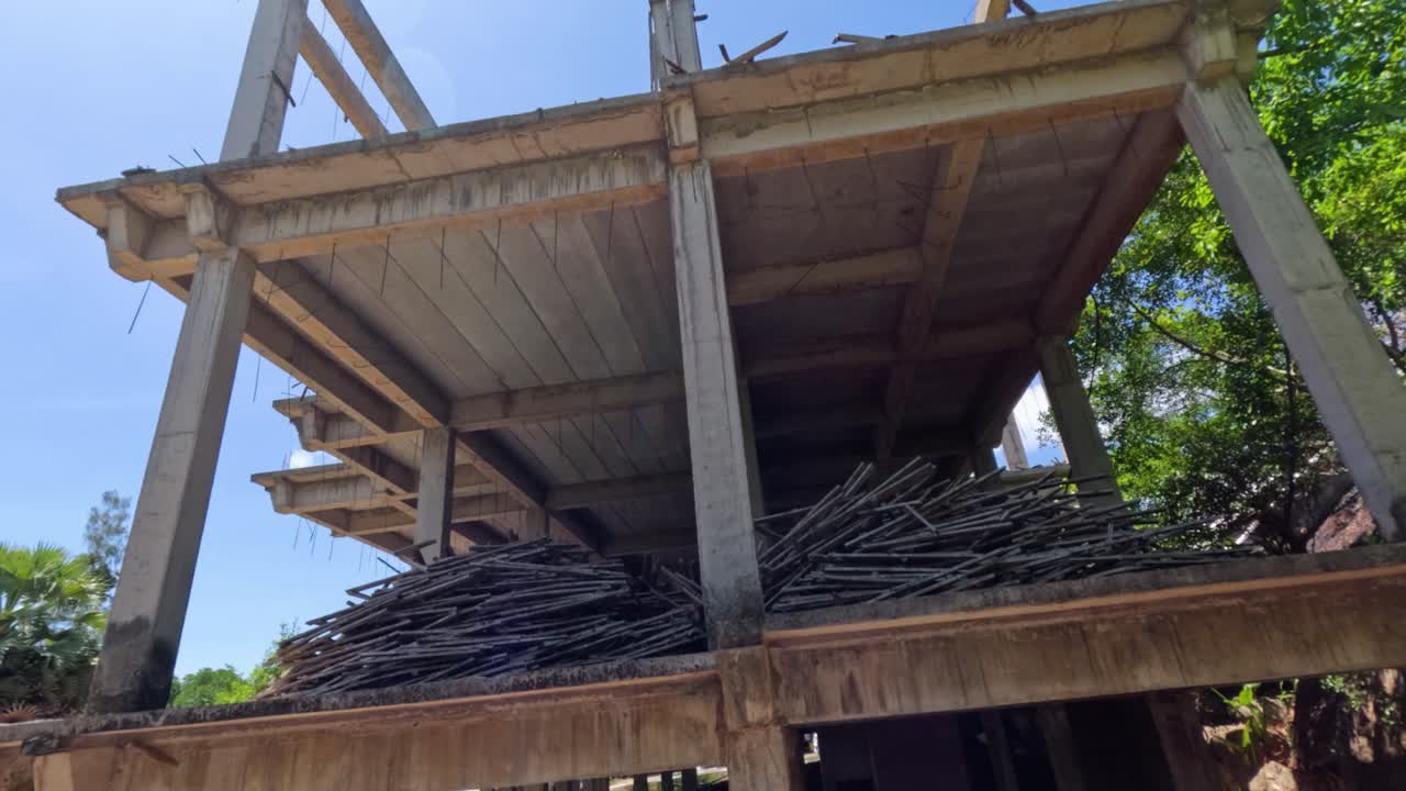 Concrete structure under construction surrounded by lush trees, sunlight, and blue sky