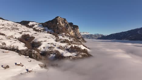 aerial view of amden, arvenbüel, and weesen in glarus, switzerland, where snow-covered slopes lead down to the fog-blanketed waters of lake walensee, framed by towering mountains and clear skies.