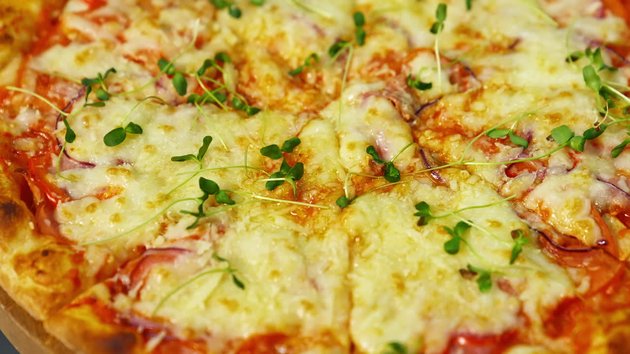 Delicious pizza. Melted cheese and green sprouts on pizza. Appetizing pizza spinning on the table. Close-up.