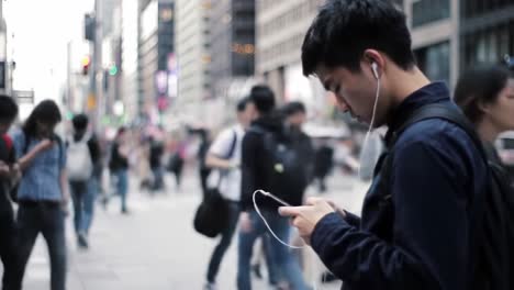 a busy urban scene captured in two frames: the focus of a young man engaged with his smartphone amidst a crowded city street