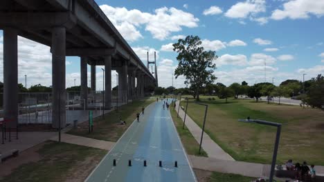 vuelo de drones con vista a la avenida con ciclistas al lado del puente sobre el río paraná en rosario argentina.