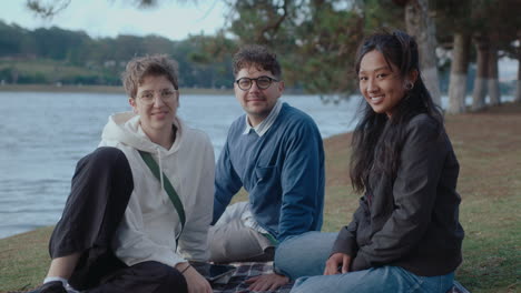 students sitting in the park and smiling on camera